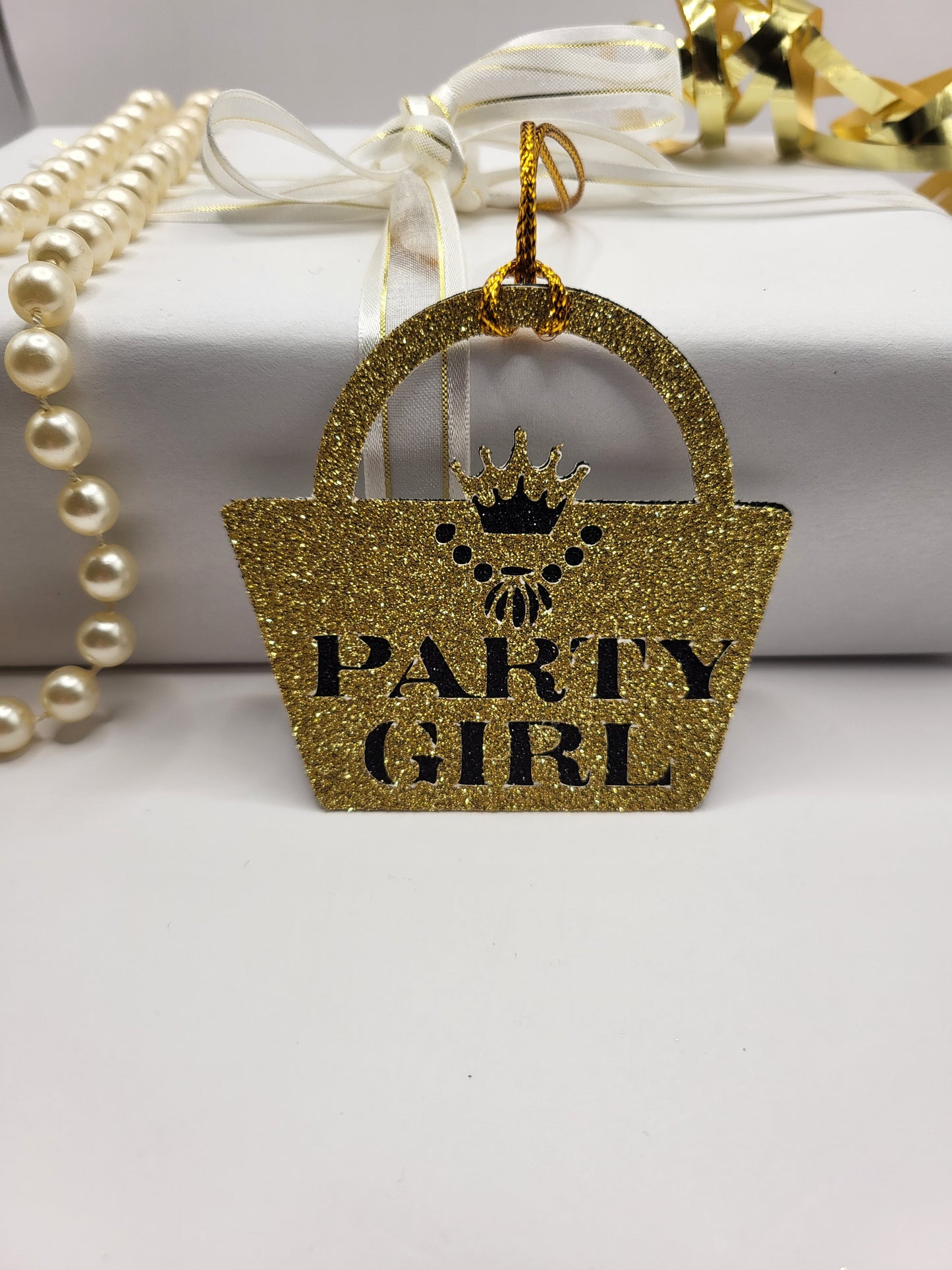 Gold glitter card handbag shaped gift tag stuck to a black glitter background. The words party girl are cut out of the gold glitter card and shows the black glitter underneath. The handbag clasp is the shape of the crown and there is a necklace cut out under the crown