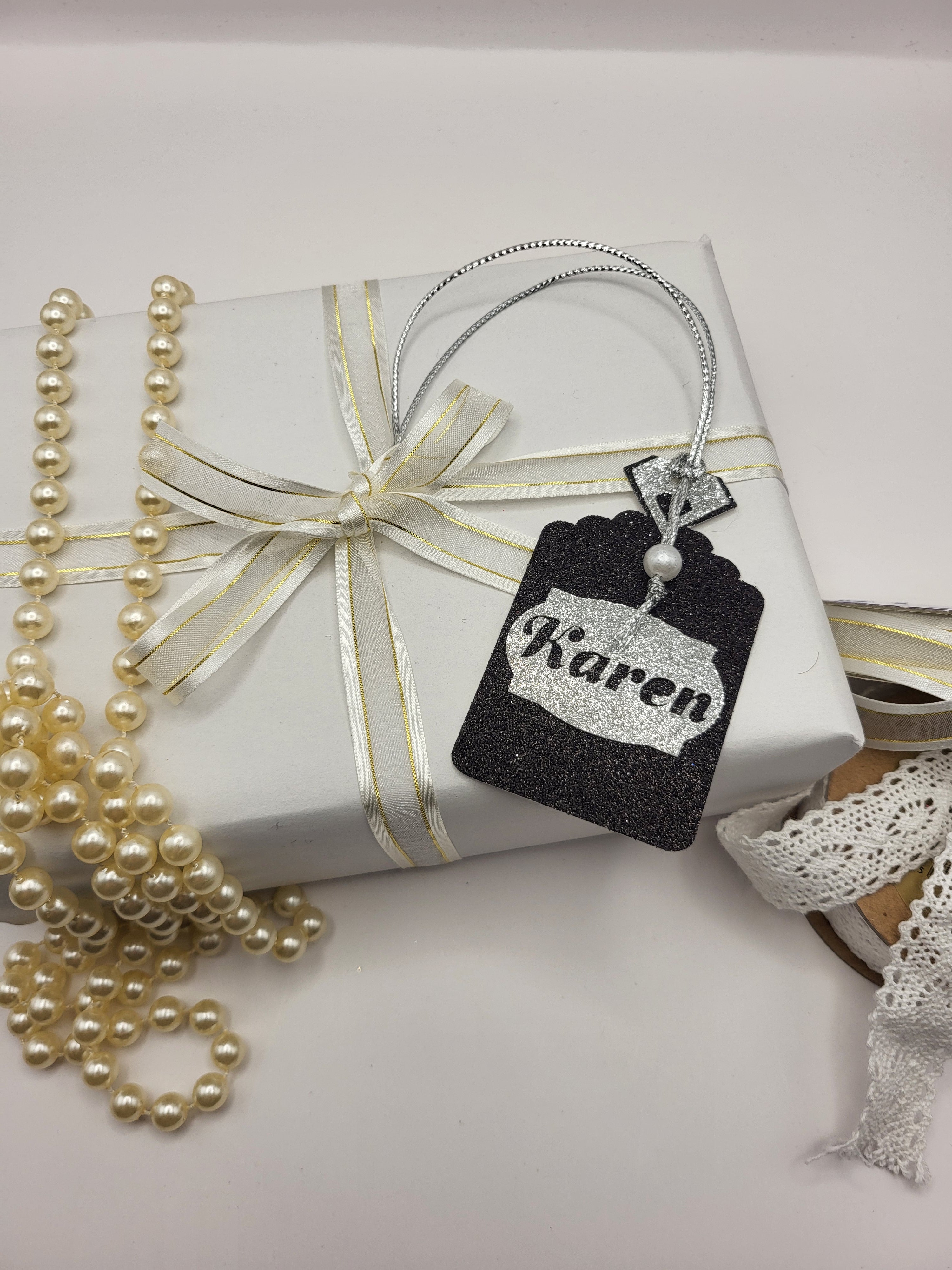 Black glitter card Perfume bottle shape gift tag has a silver tag shape stuck on the front with the chance to personalise it with the name of your choice. The bottle top is also silver glitter card with a metallic silver cord attached
