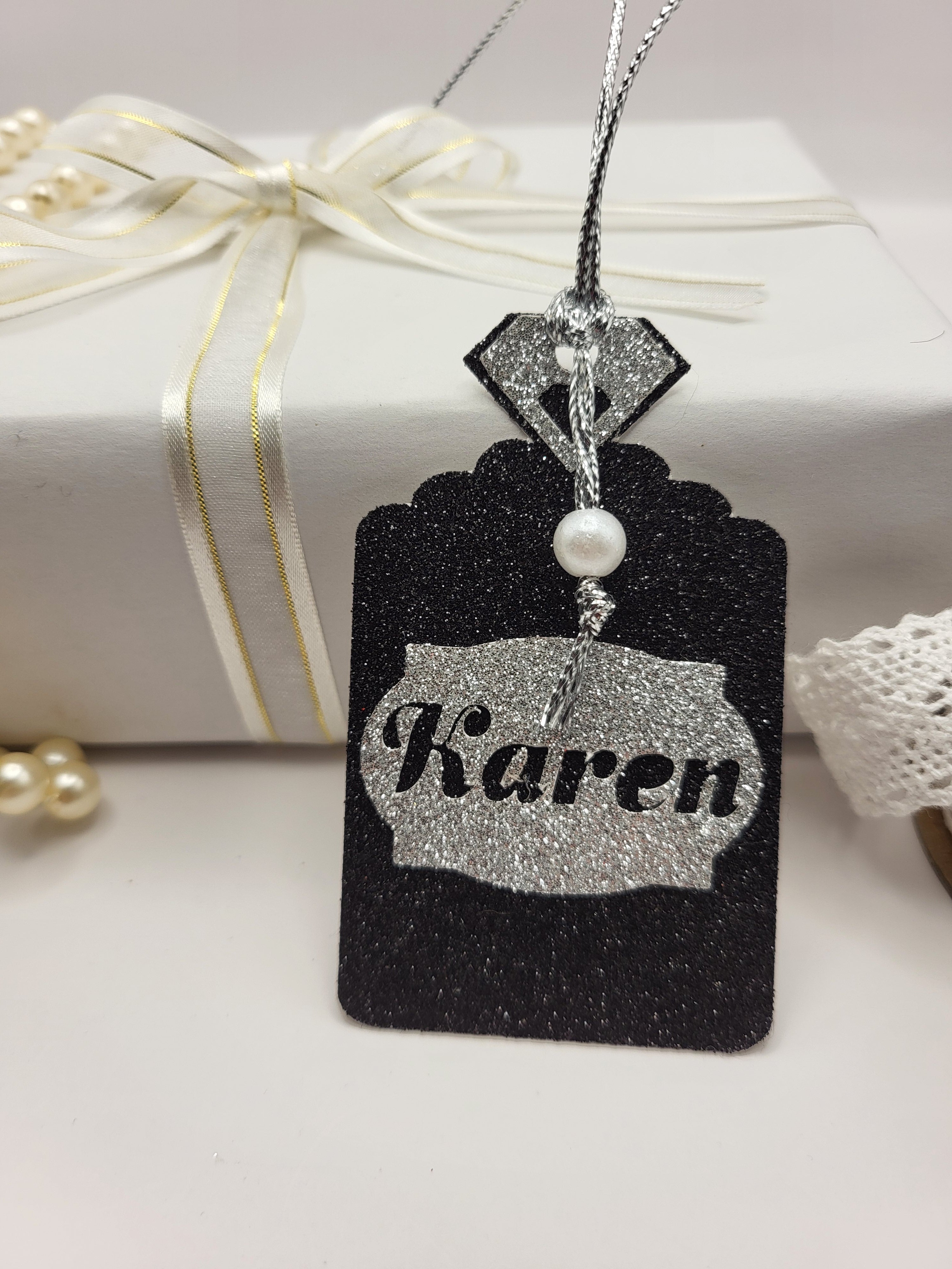Black glitter card Perfume bottle shape gift tag has a silver tag shape stuck on the front with the chance to personalise it with the name of your choice. The bottle top is also silver glitter card with a metallic silver cord attached