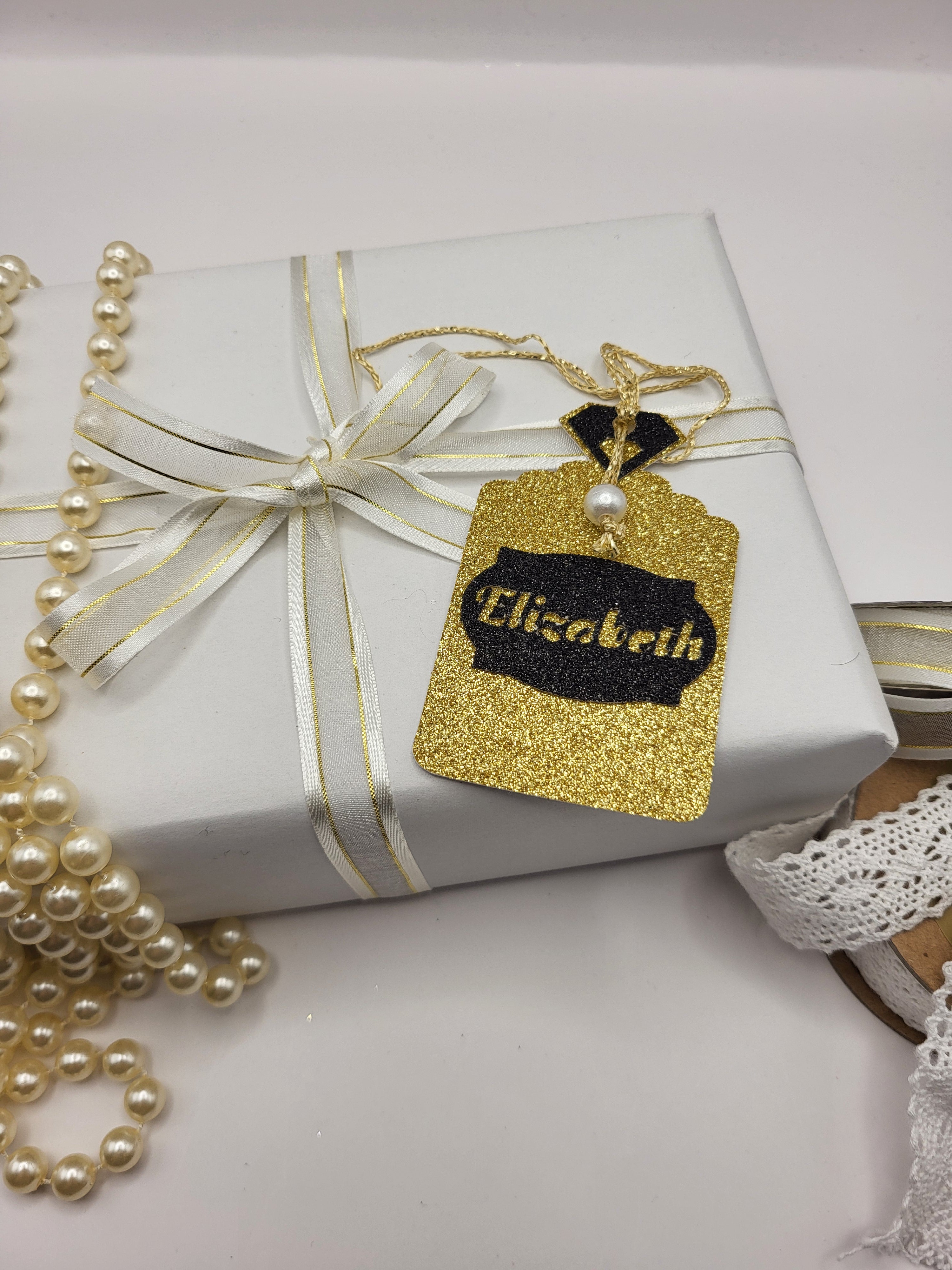 Gold glitter card Perfume bottle shape gift tag has a black tag shape stuck on the front with the chance to personalise it with the name of your choice. The bottle top is also black glitter card with a metallic gold cord attached