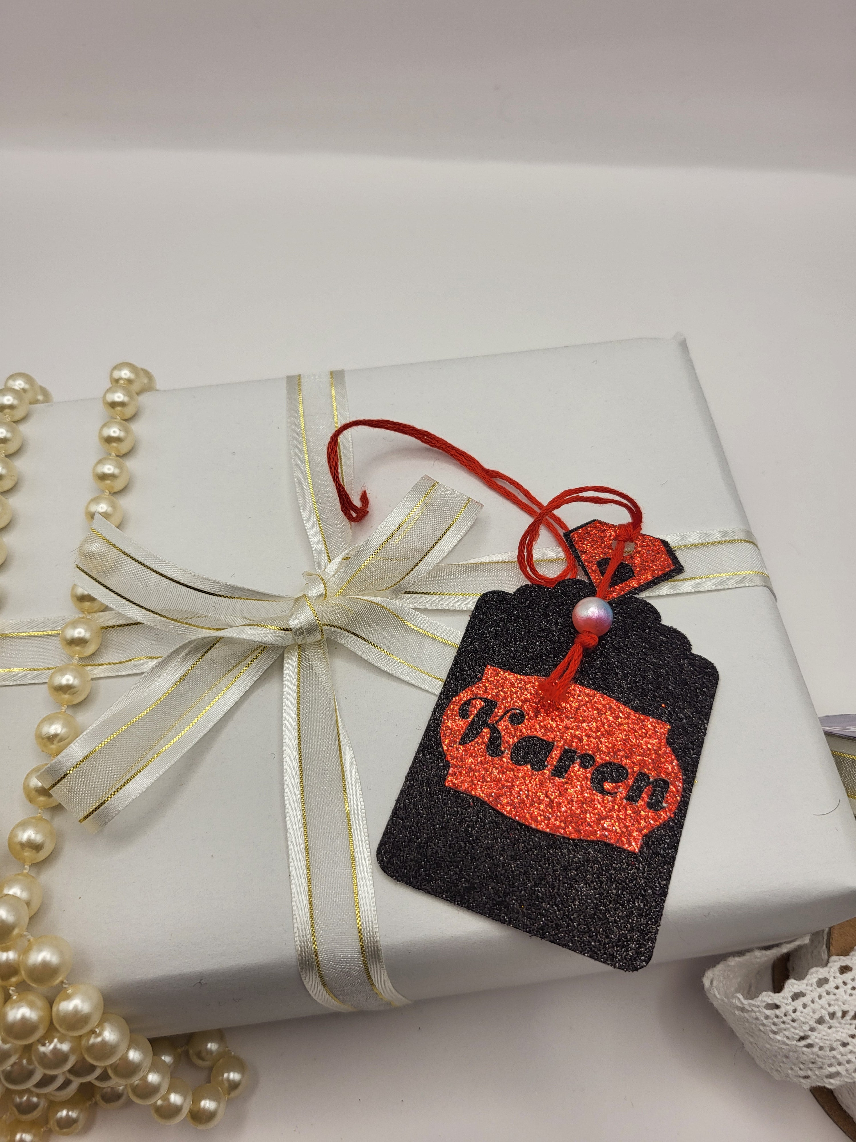 Black glitter card Perfume bottle shape gift tag has a red tag shape stuck on the front with the chance to personalise it with the name of your choice. The bottle top is also red glitter card with a red silk cord attached