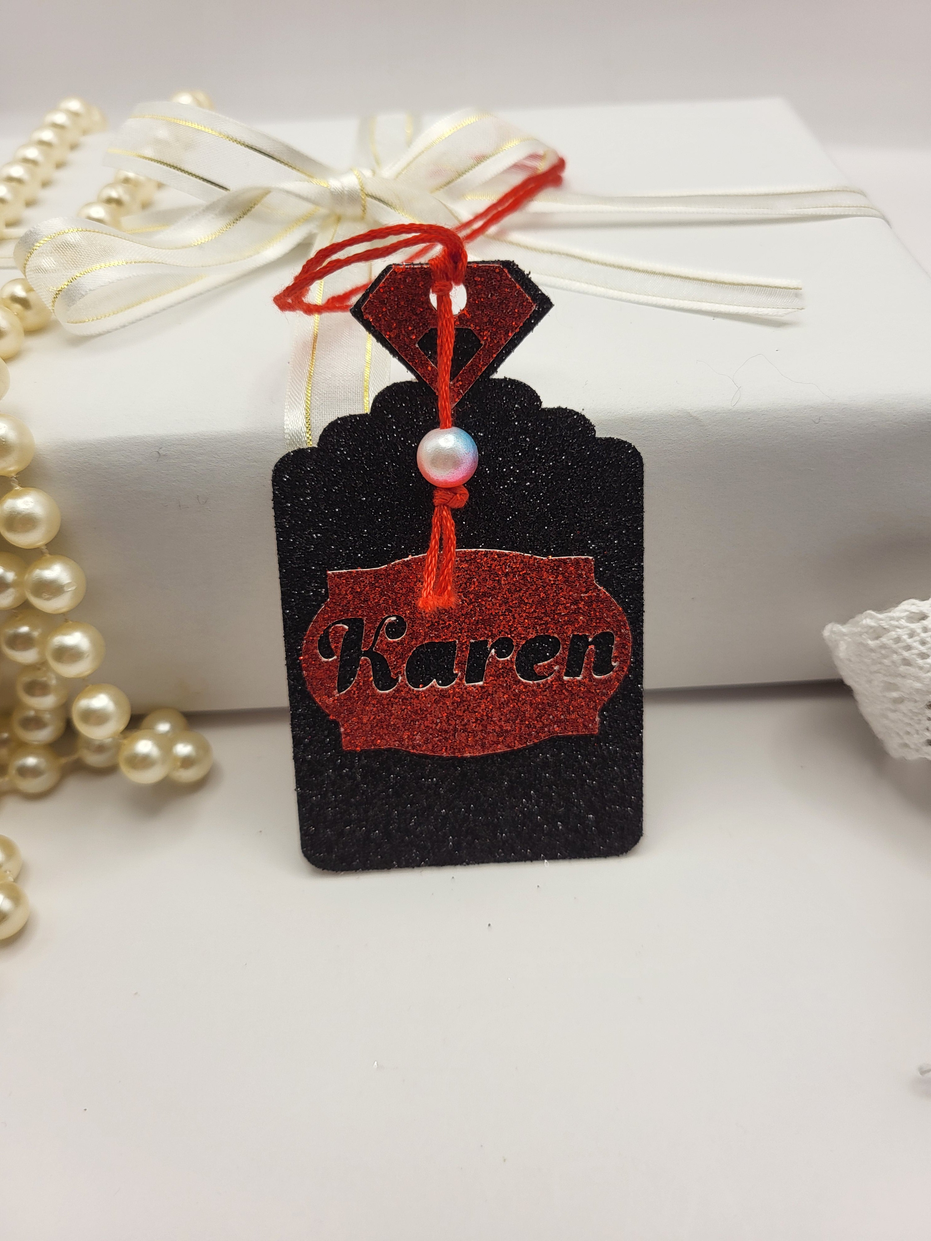 Black glitter card Perfume bottle shape gift tag has a red tag shape stuck on the front with the chance to personalise it with the name of your choice. The bottle top is also red glitter card with a red silk cord attached