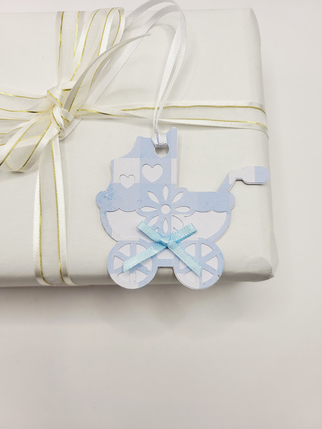 Pram shaped gift tag in blue gingham  on a white background. Pram has a blue bow and a white satin ribbon to attach the tag