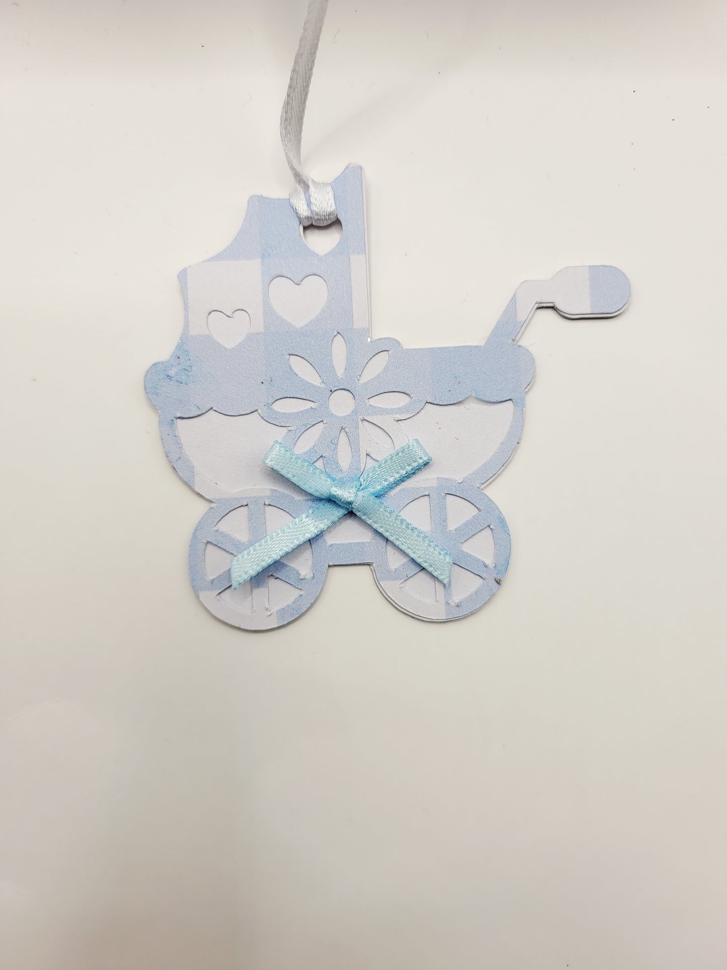 Pram shaped gift tag in blue gingham  on a white background. Pram has a blue bow and a white satin ribbon to attach the tag