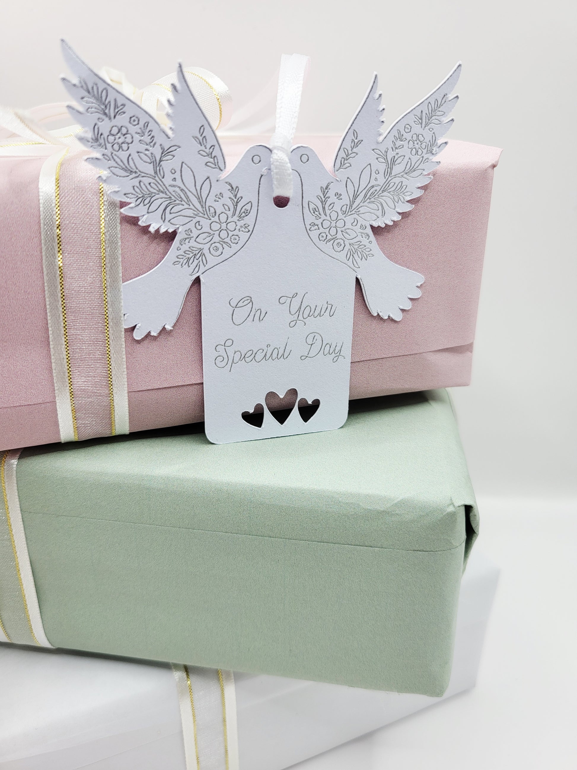 A white card gift tag with the words On Your Special Day foiled in silver. There are tow doves one each side of the tag near the top. The pattern on the wings are also foiled. There are 3 love hearts cut out at the bottom of the tag and it is blank on the reverse 
