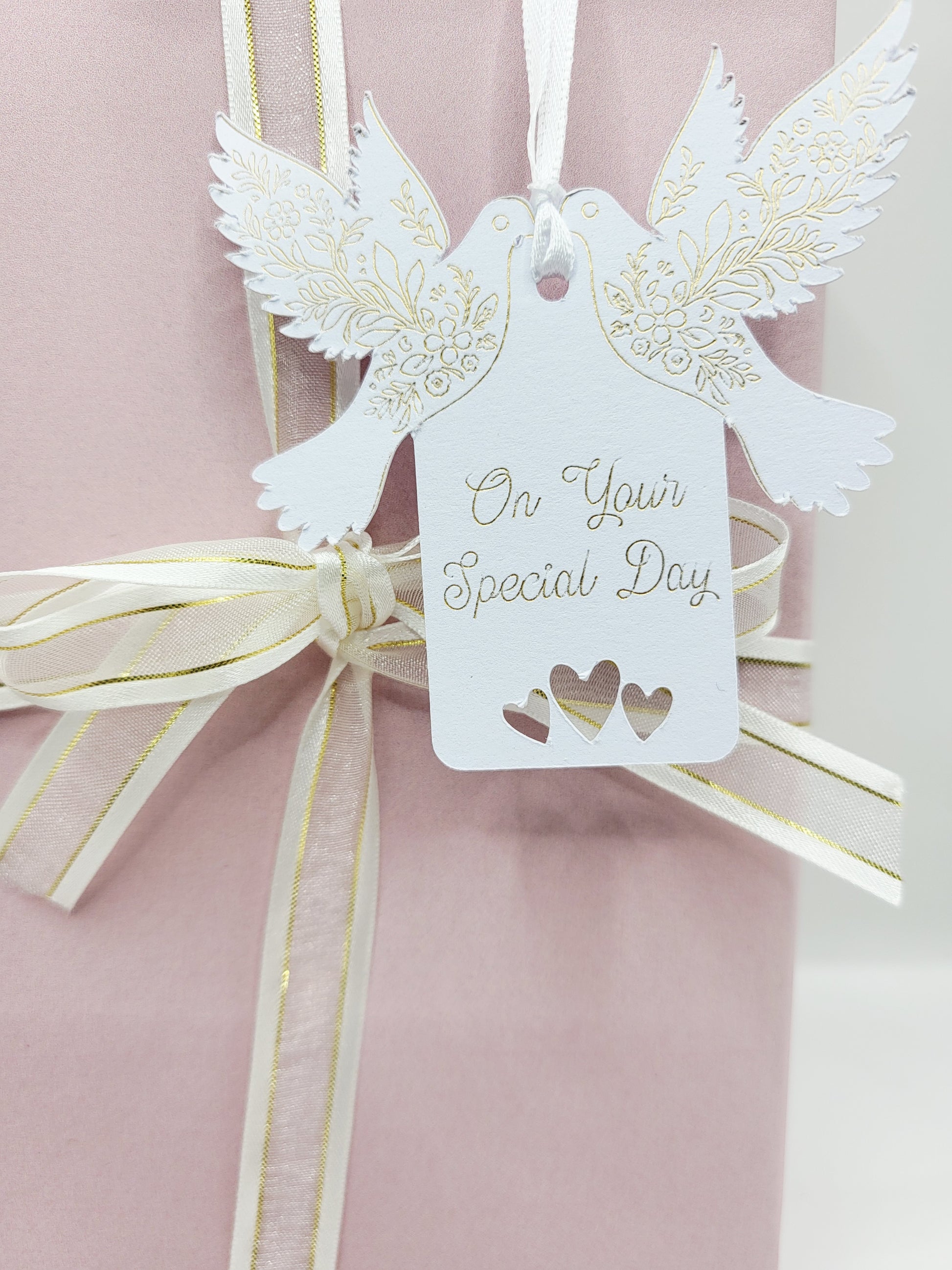 A white card gift tag with the words On Your Special Day foiled in gold. There are tow doves one each side of the tag near the top. The pattern on the wings are also foiled. There are 3 love hearts cut out at the bottom of the tag and it is blank on the reverse 