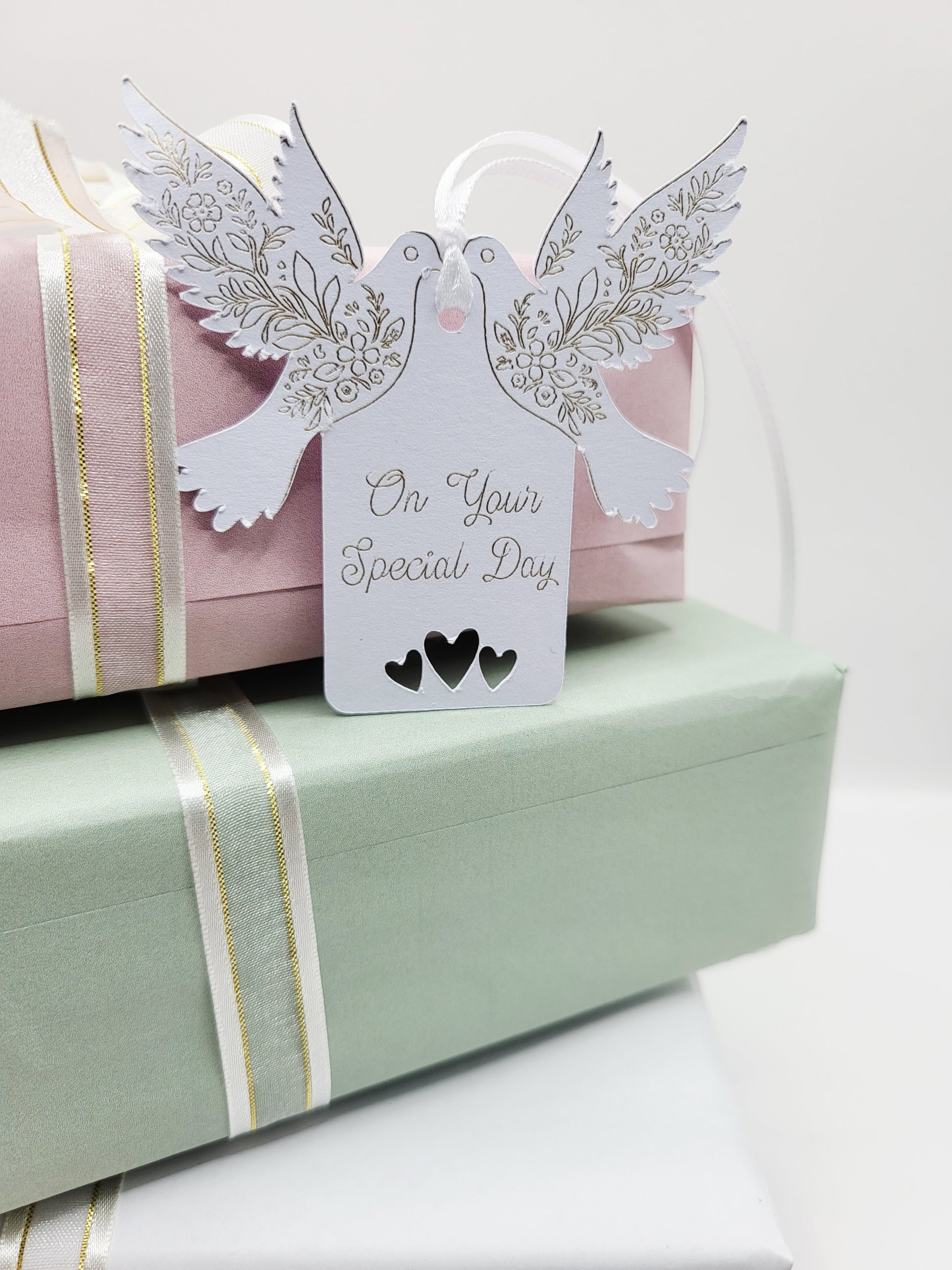 A white card gift tag with the words On Your Special Day foiled in gold. There are tow doves one each side of the tag near the top. The pattern on the wings are also foiled. There are 3 love hearts cut out at the bottom of the tag and it is blank on the reverse 