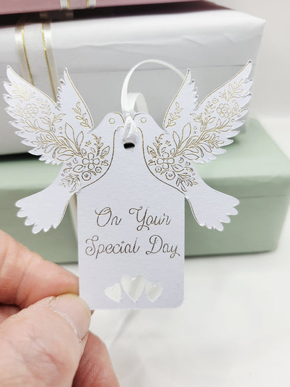 A white card gift tag with the words On Your Special Day foiled in silver. There are tow doves one each side of the tag near the top. The pattern on the wings are also foiled. There are 3 love hearts cut out at the bottom of the tag and it is blank on the reverse 