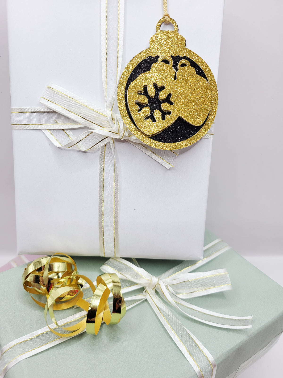 Christmas Bauble shape gift tag has a black glitter background with a gold glitter edge around the bauble and two baubles in gold glitter cardstock in the centre of the bauble. The back is blank and the tag has a gold metallic cord to attach to your gift.