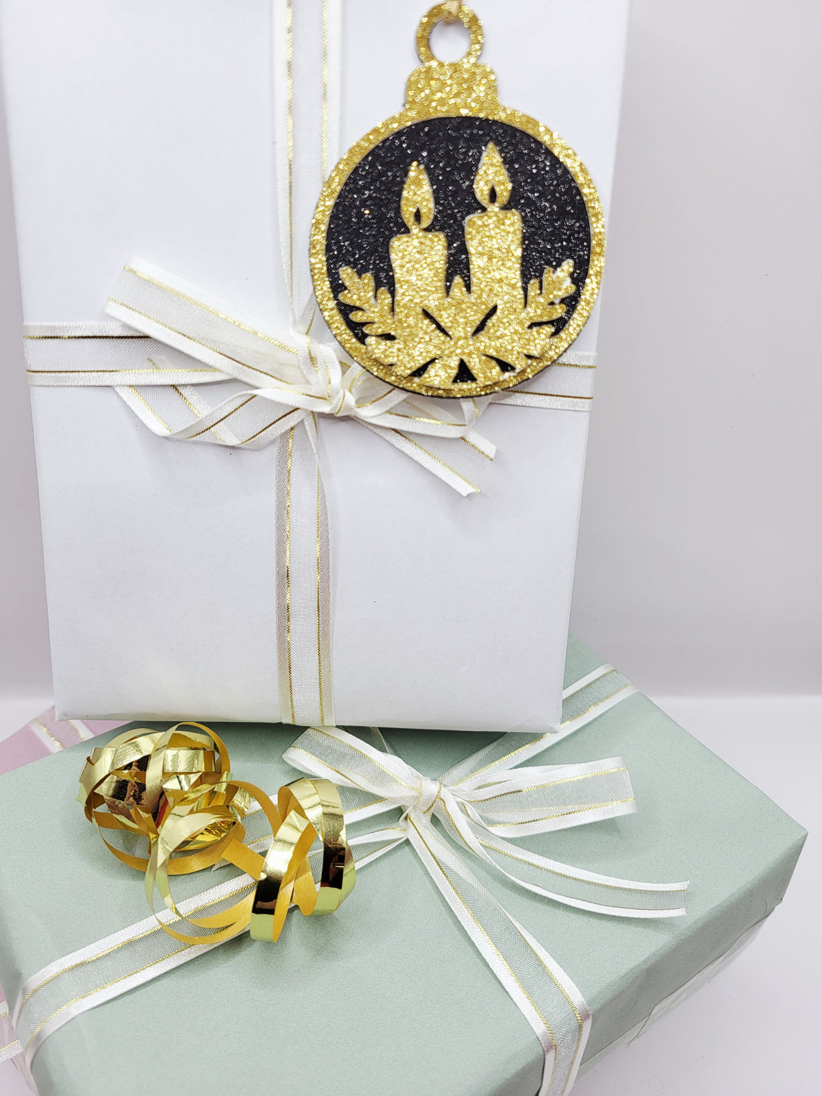 Christmas Bauble shape gift tag has a black glitter background with a gold glitter edge around the bauble and two candles sat on holly in gold glitter cardstock at the bottom of the bauble. The back is blank and the tag has a gold metallic cord to attach to your gift.
