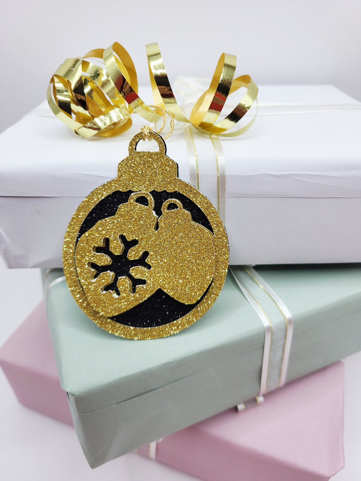 Christmas Bauble shape gift tag has a black glitter background with a gold glitter edge around the bauble and two baubles in gold glitter cardstock in the centre of the bauble. The back is blank and the tag has a gold metallic cord to attach to your gift.
