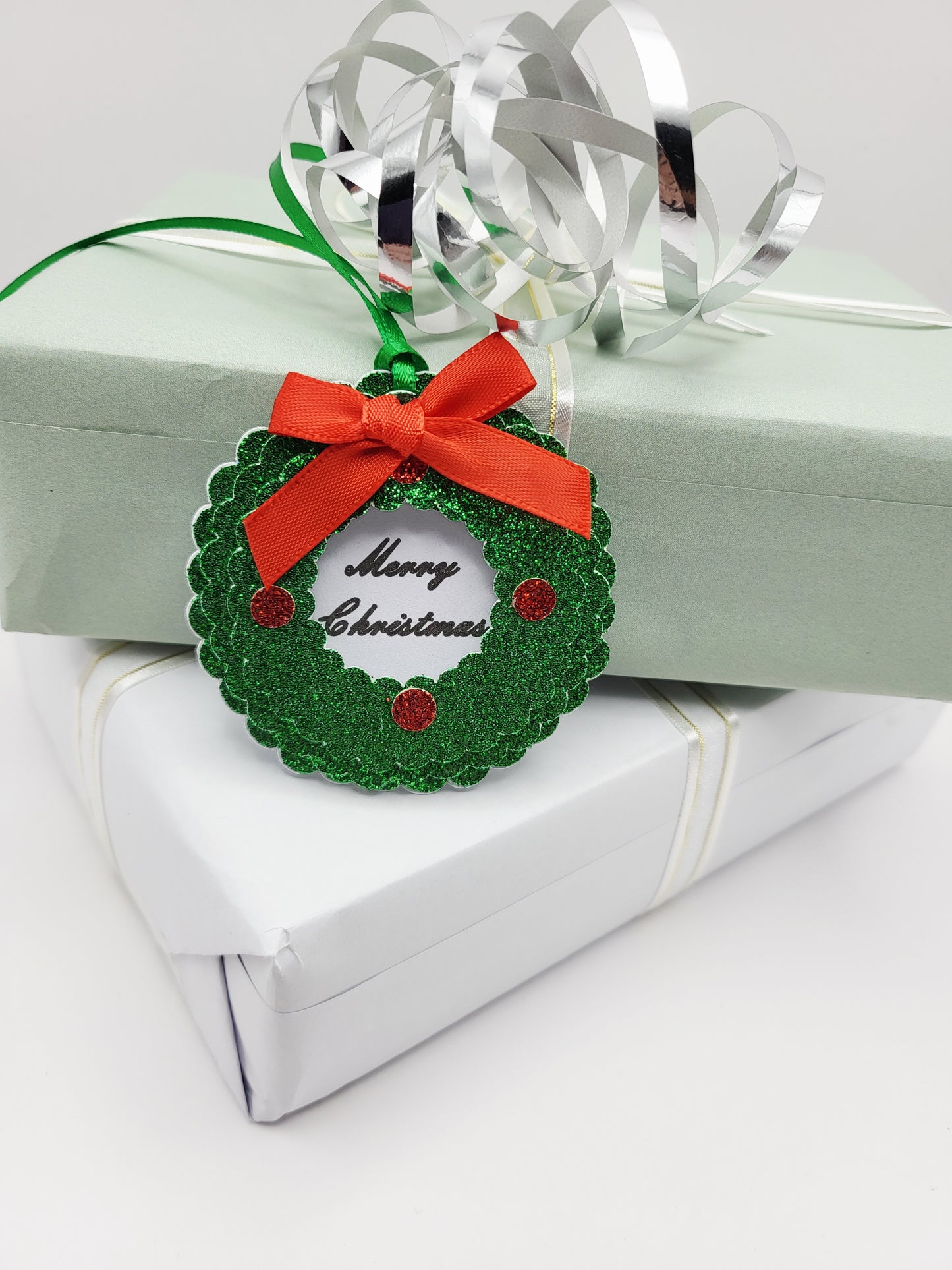 A green glitter Christmas wreath gift tag with a red ribbon bow and 'Merry Christmas' text,