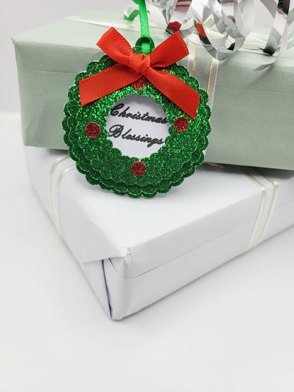 A green glitter Christmas wreath gift tag with a red ribbon bow and 'Christmas Blessings' text, in the centre on a white card background