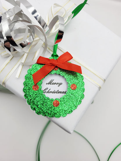 A green glitter Christmas wreath gift tag with a red ribbon bow and 'Merry Christmas' text, in the centre on a white card background
