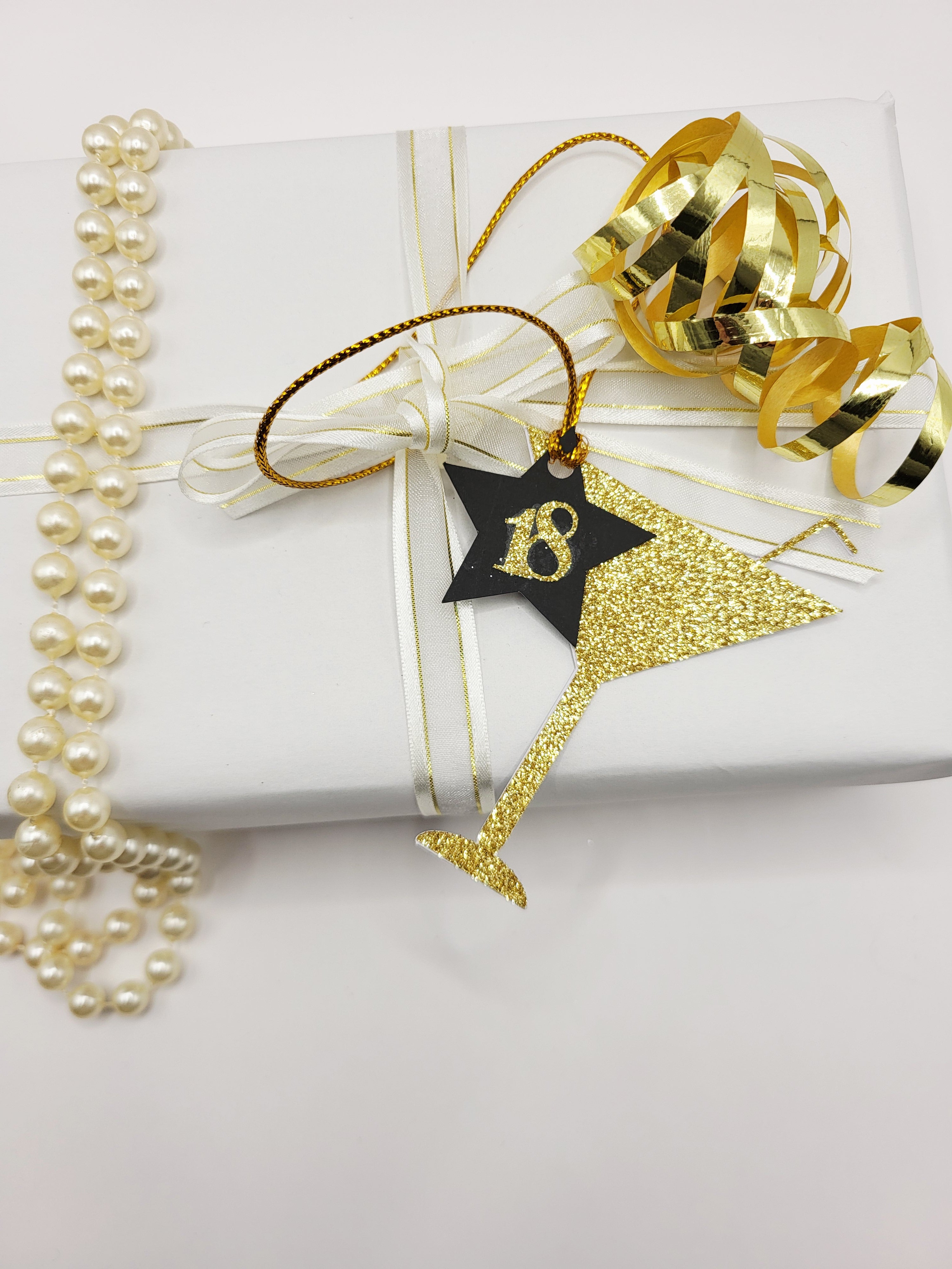 Gold glitter milestone age cocktail shaped gift tag. The glass shape has a straw sticking from the top.
There is a black card star with the milestone age in gold glitter stuck on the star and hung from the glass. The tag has a gold metallic cord attached so you can attach your gift easily