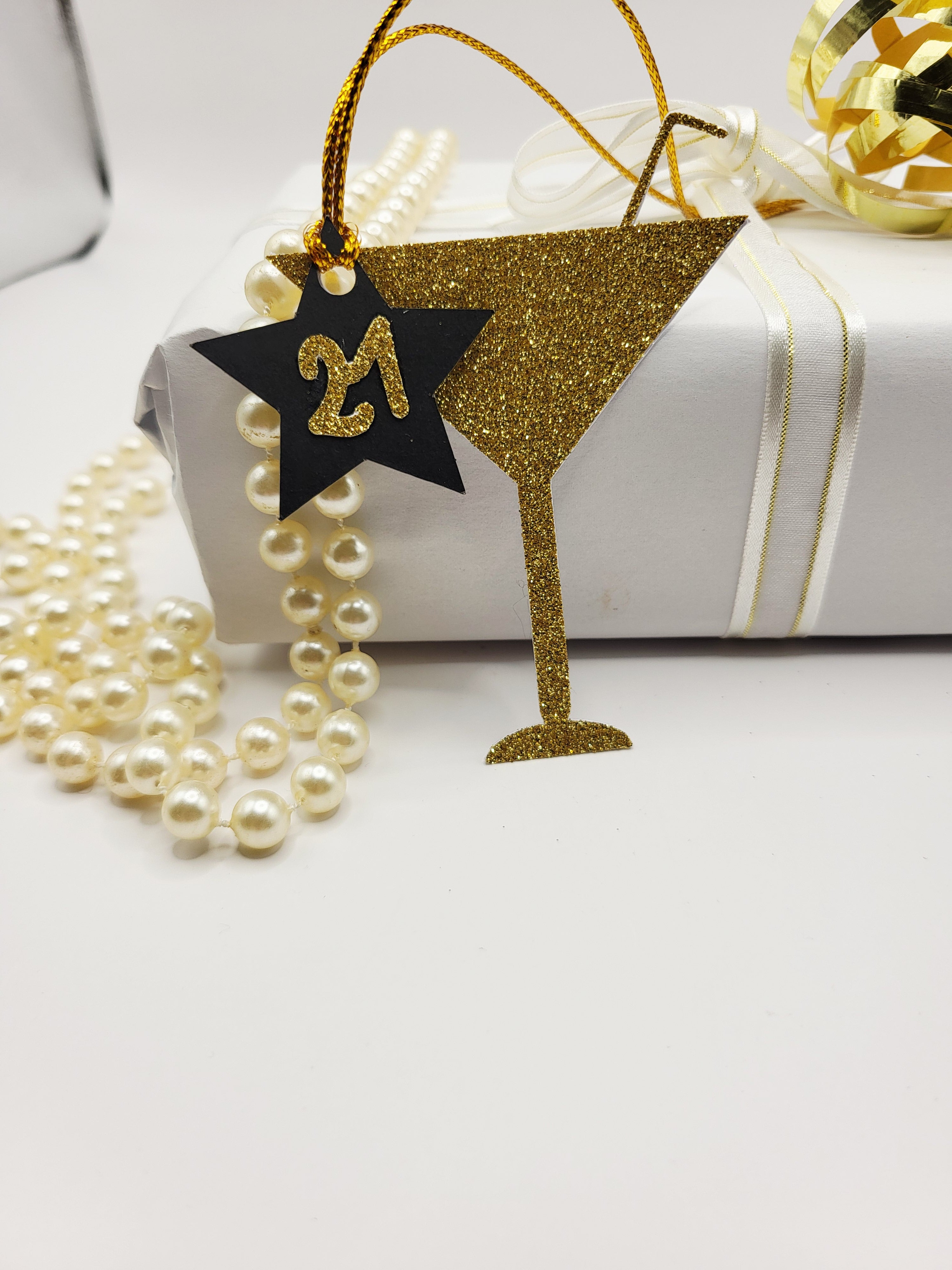 Gold glitter milestone age cocktail shaped gift tag. The glass shape has a straw sticking from the top.
There is a black card star with the milestone age in gold glitter stuck on the star and hung from the glass. The tag has a gold metallic cord attached so you can attach your gift easily