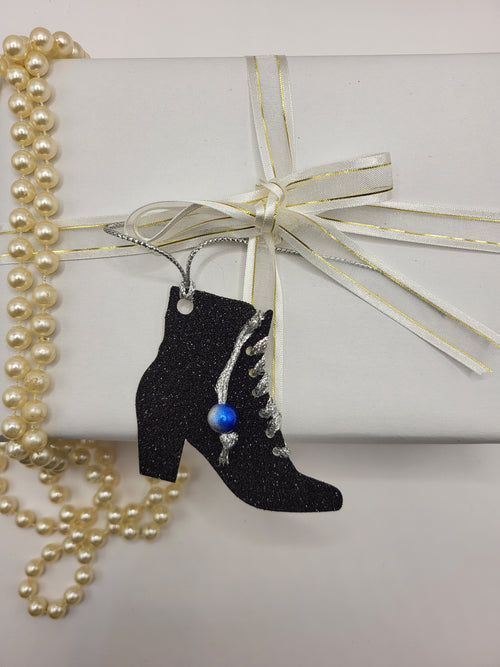 This is a black glitter ankle boot shaped gift tag with silver metallic cord threaded through the eyelets with a blue pearl hanging from the thread.