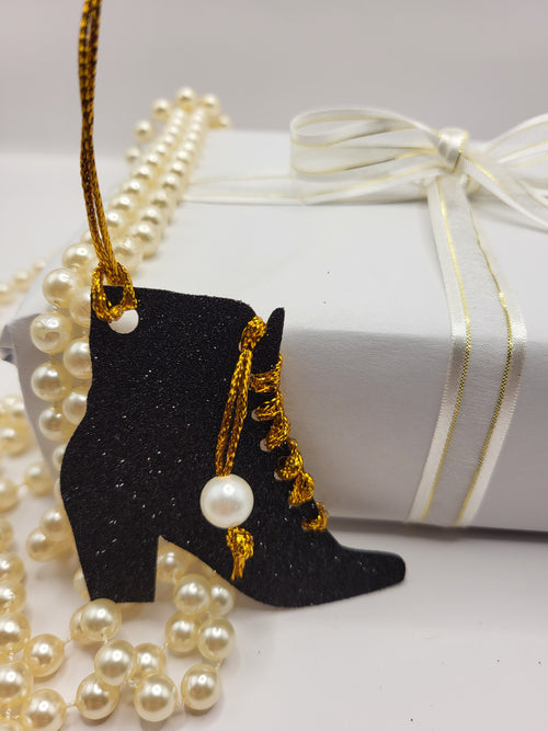 This is a black glitter ankle boot shaped gift tag with gold metallic cord threaded through the eyelets with a white pearl hanging from the thread.