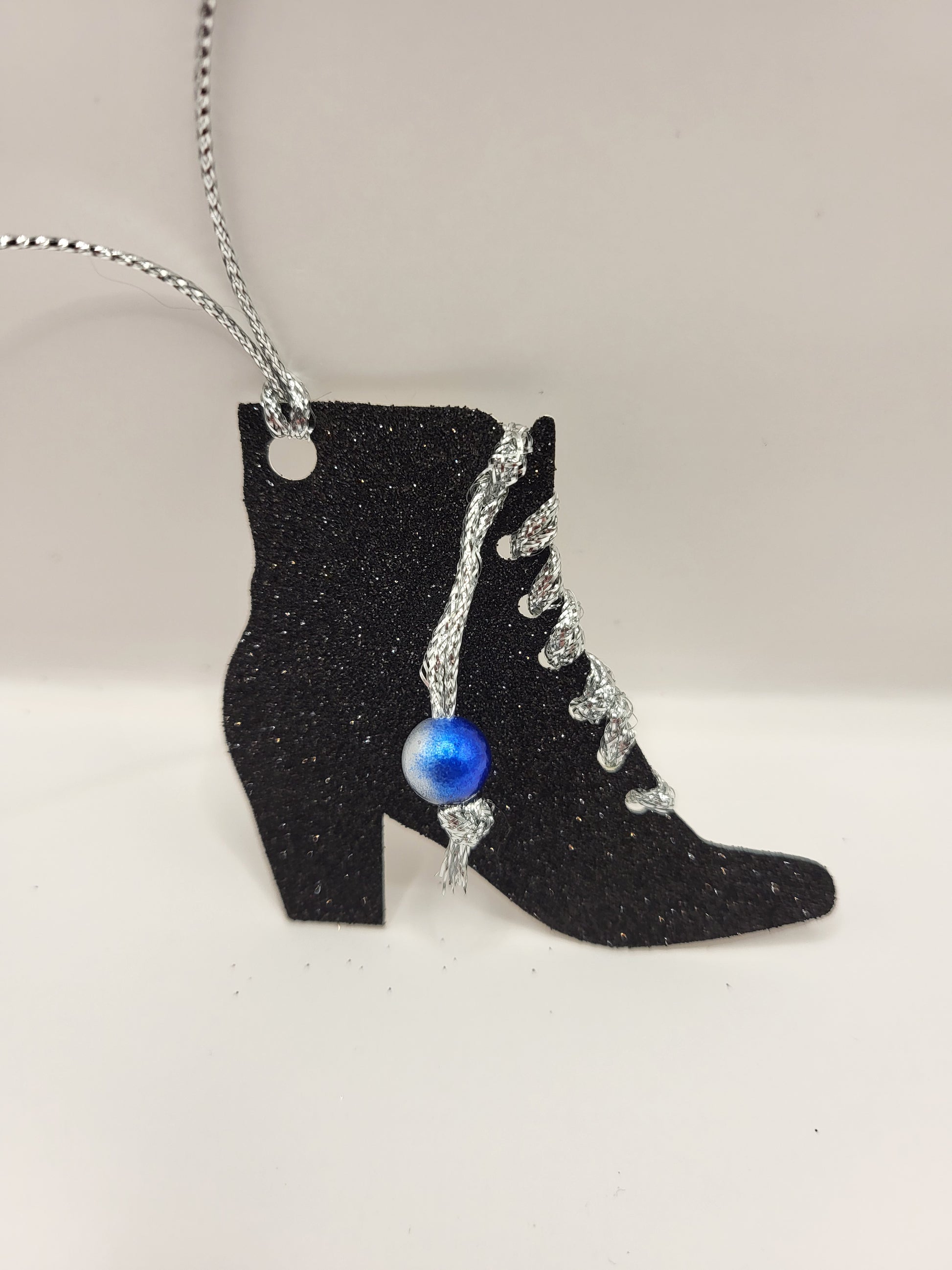 This is a black glitter ankle boot shaped gift tag with silver metallic cord threaded through the eyelets with a blue pearl hanging from the thread.
