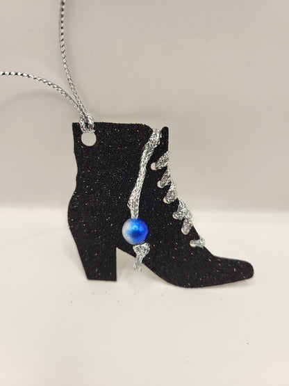 This is a black glitter ankle boot shaped gift tag with silver metallic cord threaded through the eyelets with a blue pearl hanging from the thread.