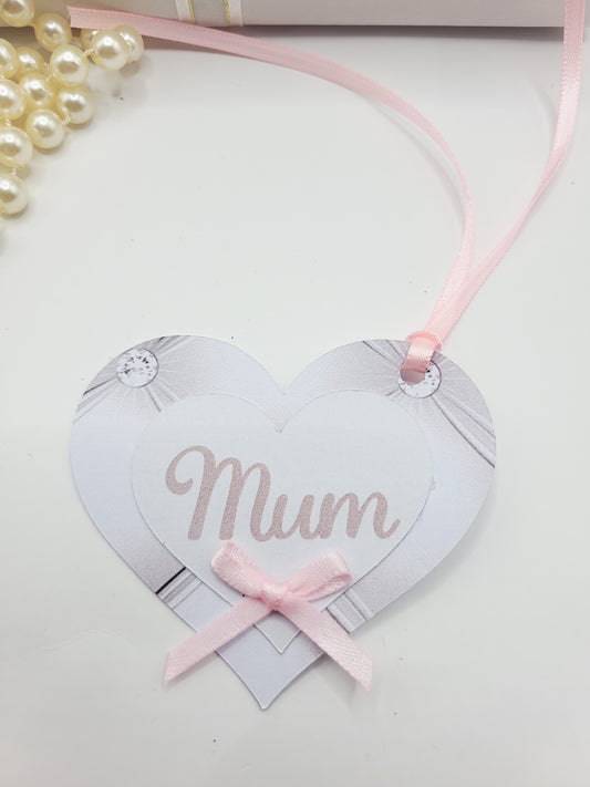 Heart shape gift tag with printed pink pearl background. There is a smaller white heart on top with the word mum printed on it. There is a small pink bow under the word mum