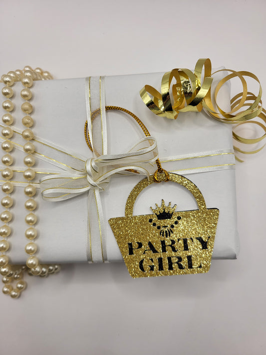 Gold glitter card handbag shaped gift tag stuck to a black glitter background. The words party girl are cut out of the gold glitter card and shows the black glitter underneath. The handbag clasp is the shape of the crown and there is a necklace cut out under the crown