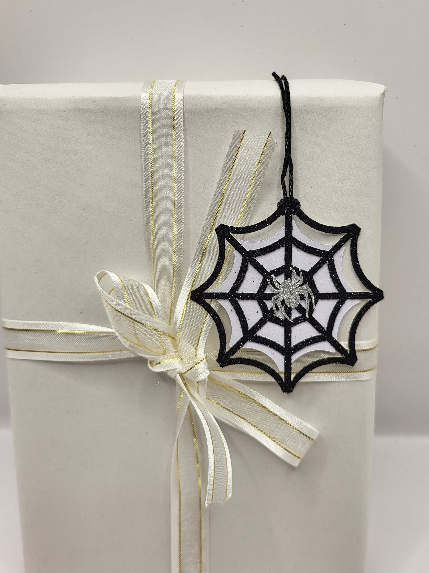 Black glitter spiderweb gift tag with a silver glitter spider stuck in the middle