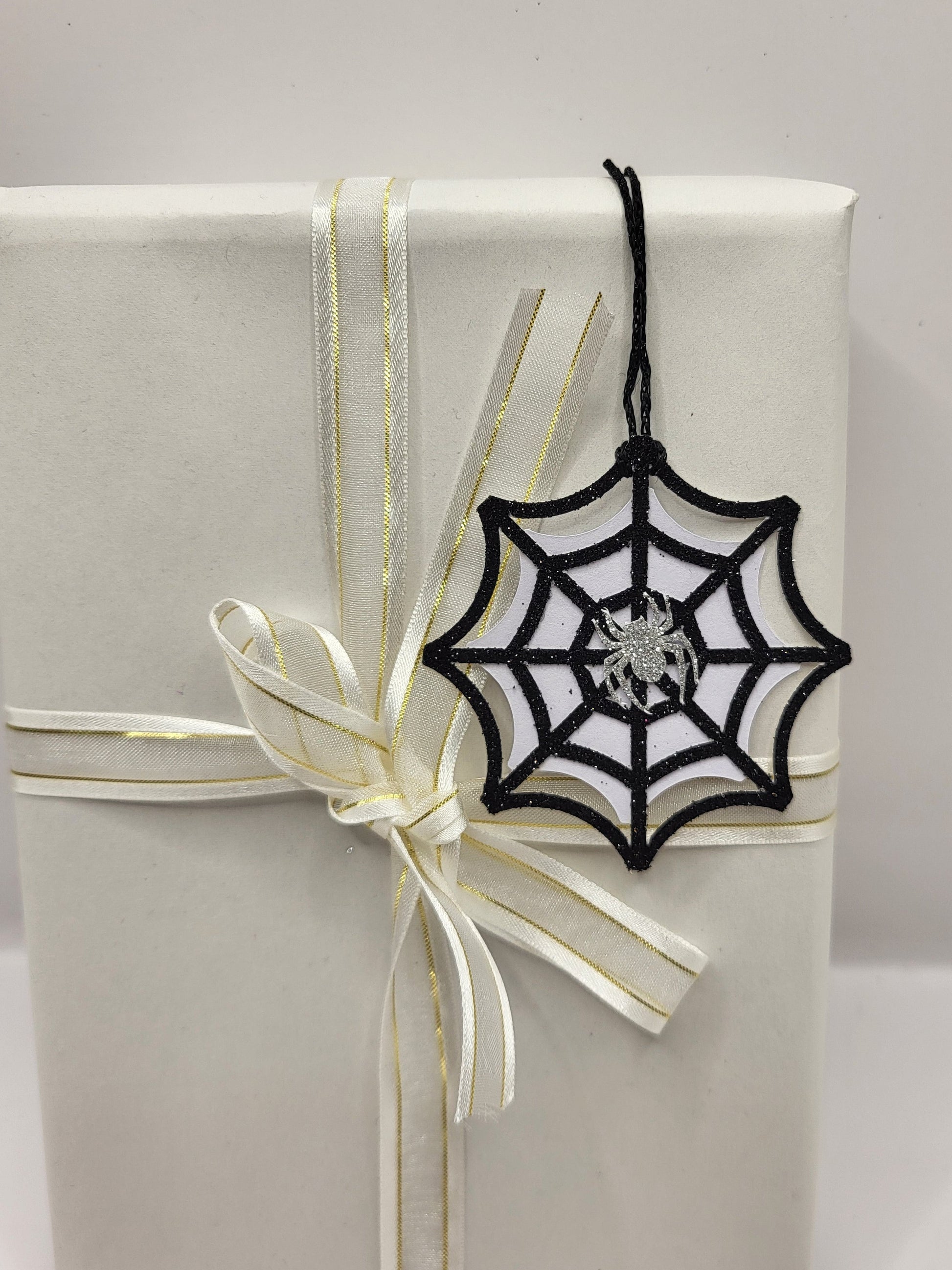 Black glitter spiderweb gift tag with a silver glitter spider stuck in the middle