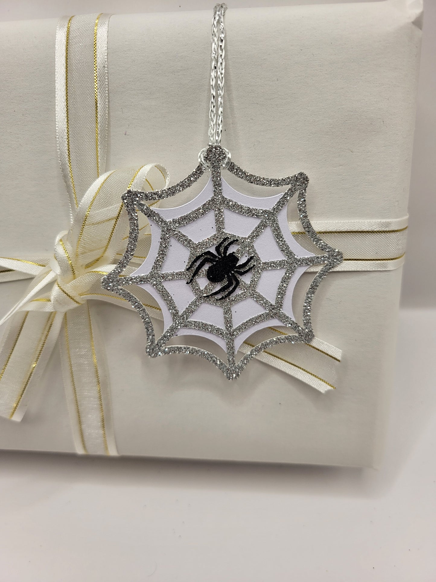 Silver glitter spiderweb gift tag. There is a black glitter spider stuck in the middle